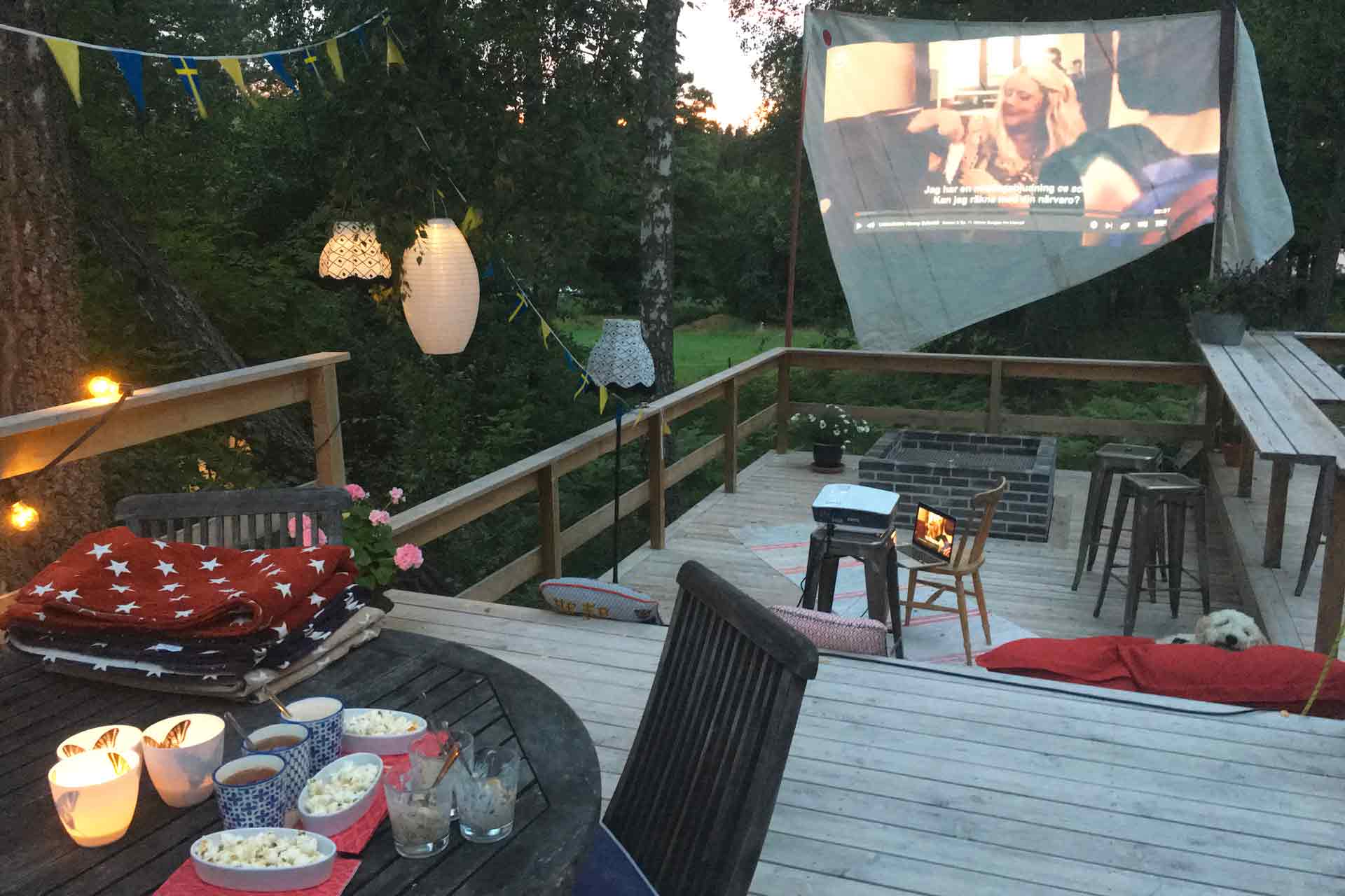 Kvällsbio utomhus på en veranda med utekök, bar och murad eldstad. Filmen visas på segelduk. Arkitekt är Anders Frelin.