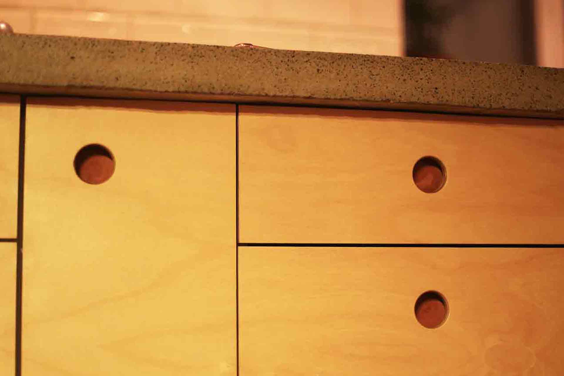 Tre hål i kökslådor i björk blir till handtag i köket ritat av arkitekt Anders Frelin. Ovanpå ligger en betongbänk.