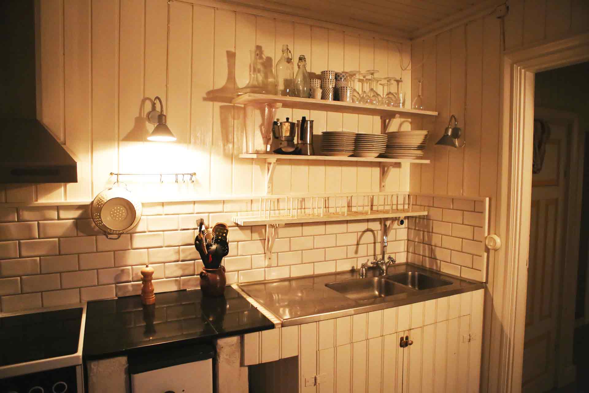Ett vitt lantkök klätt pärlspont. På väggen står porslin på hyllor ovan diskhon. Arkitekt är Anders Frelin.