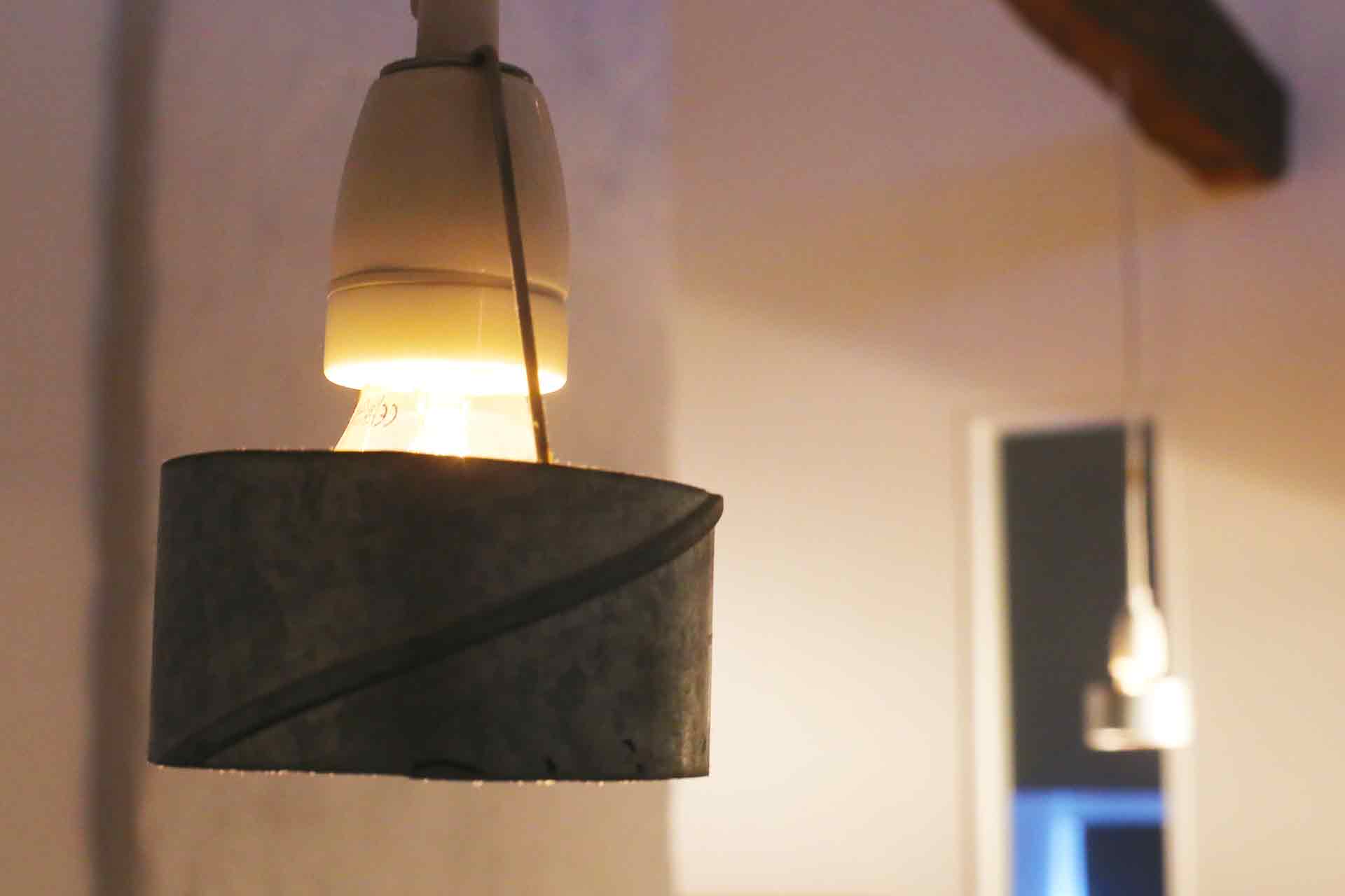 En glödlampa hänger från taket i en porslinshållare med ventilationsrör runt sig. Ljuset sprids uppåt och neråt.