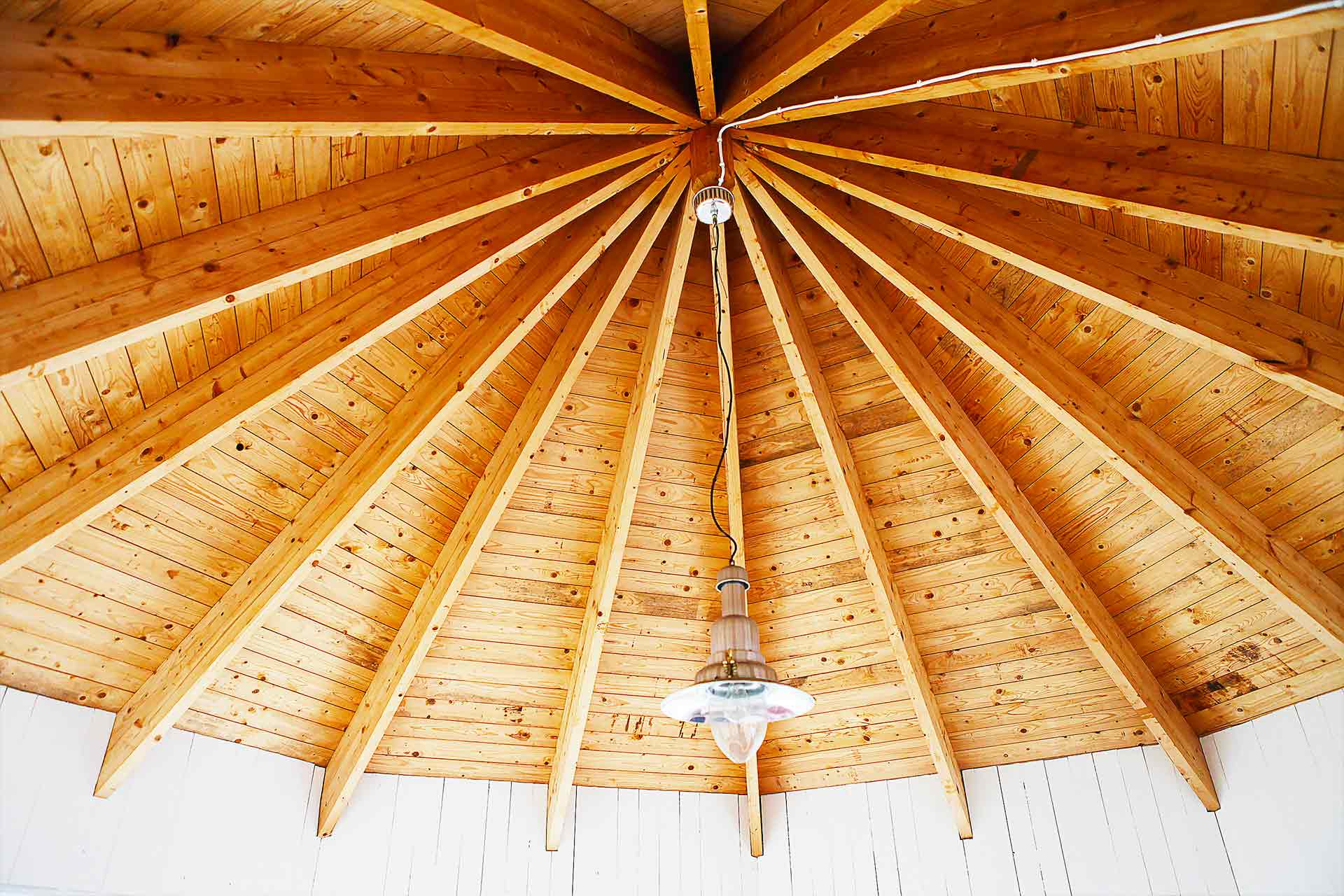Takstolar i ett åttkantigt rum strålar samman i takets mitt varifrån en metall-lampa hänger. Arkitekt är Anders Frelin.